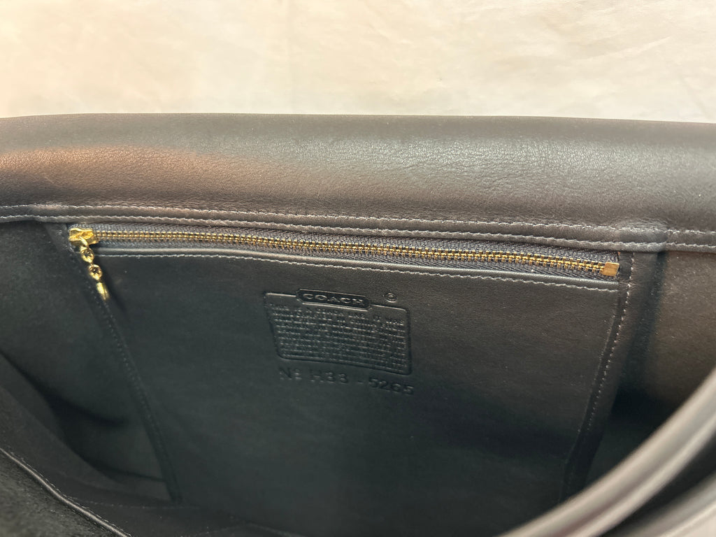 Close-up of the interior of a Coach leather bag, showing a dark brown or black leather lining with a gold zipper and a visible Coach brand label.