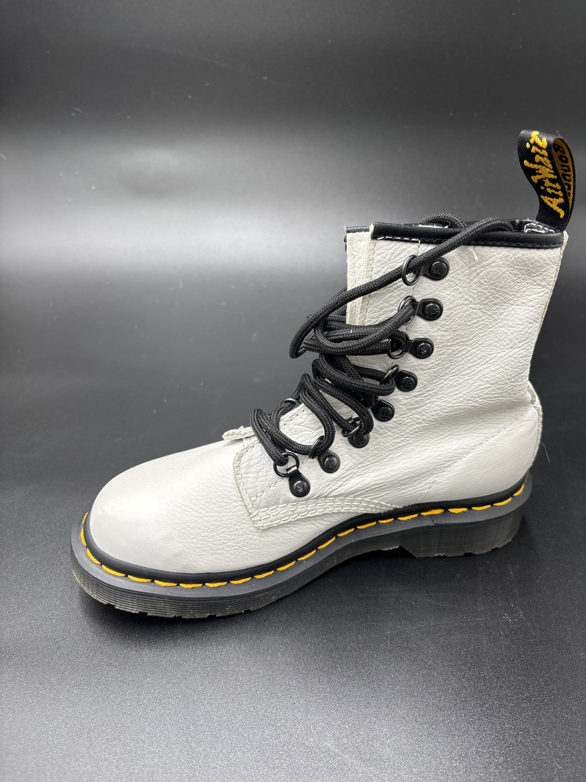 A single white leather Dr. Martens 1460 boot with black laces, black eyelets, and a signature yellow welt stitch on a dark gray background.