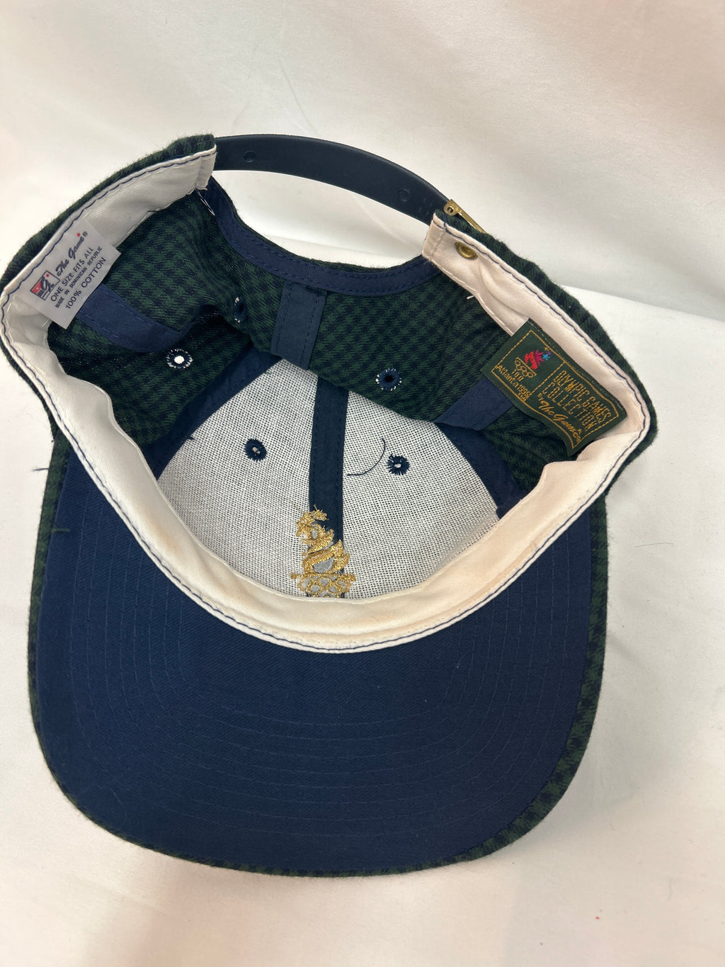 A navy blue baseball cap shown from the inside, featuring a dark green and navy checkered patterned back panel, a light gray fabric front panel with embroidered details, and a cream-colored inner lining.