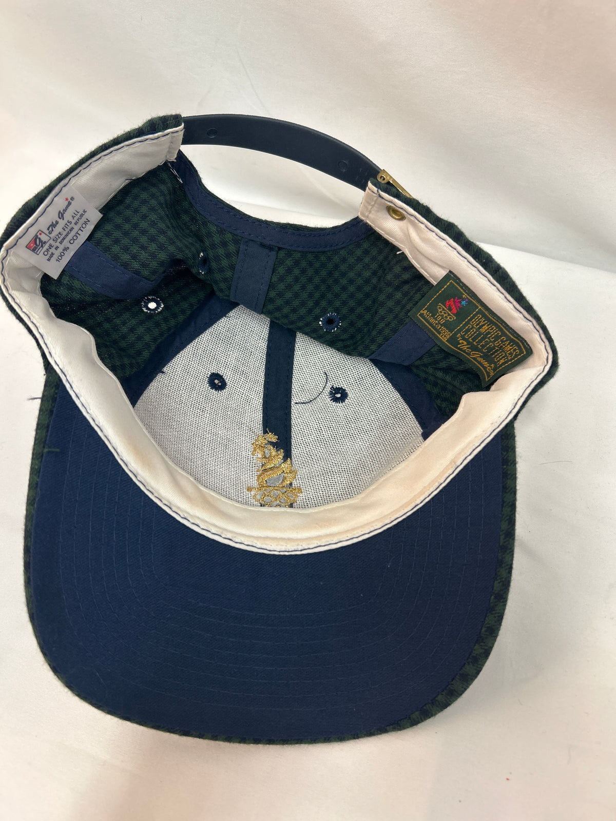 A navy blue baseball cap shown from the inside, featuring a dark green and navy checkered patterned back panel, a light gray fabric front panel with embroidered details, and a cream-colored inner lining.