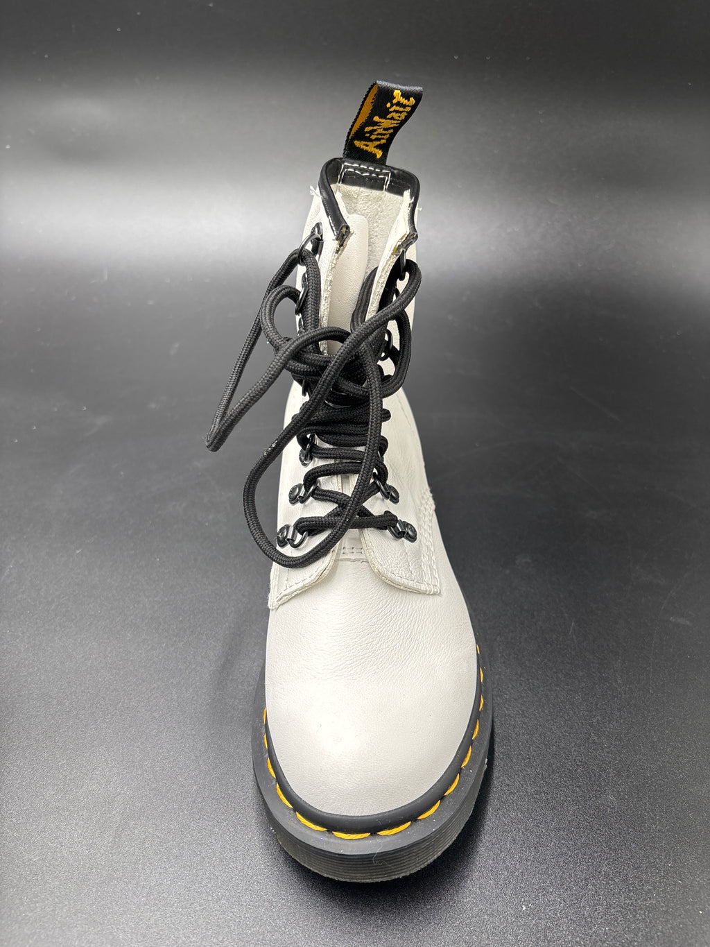 A single white leather Dr. Martens 8-eyelet lace-up boot with black laces, a black sole, and yellow stitching, photographed on a dark gray background.
