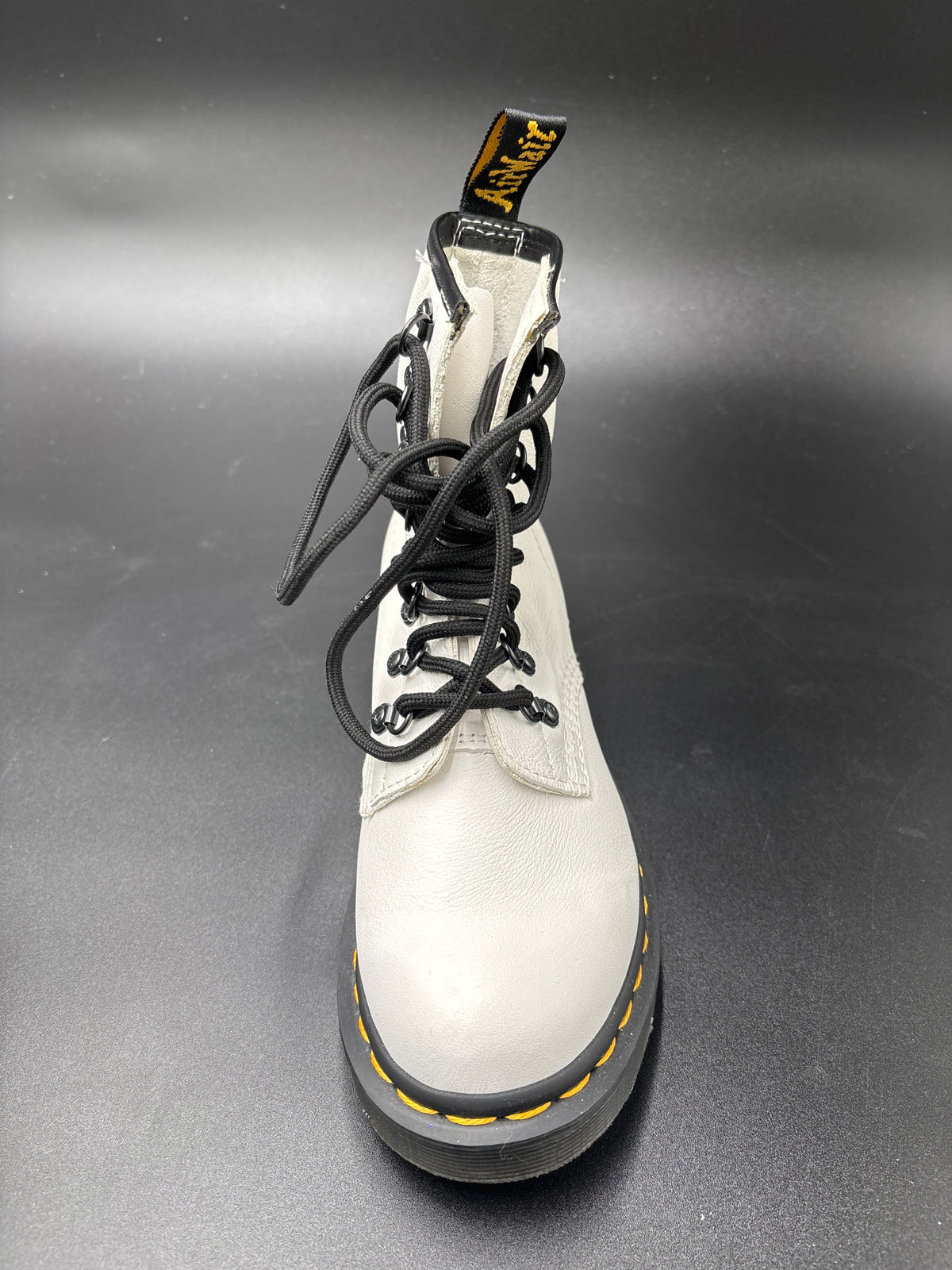 A single white leather Dr. Martens 8-eyelet lace-up boot with black laces, a black sole, and yellow stitching, photographed on a dark gray background.