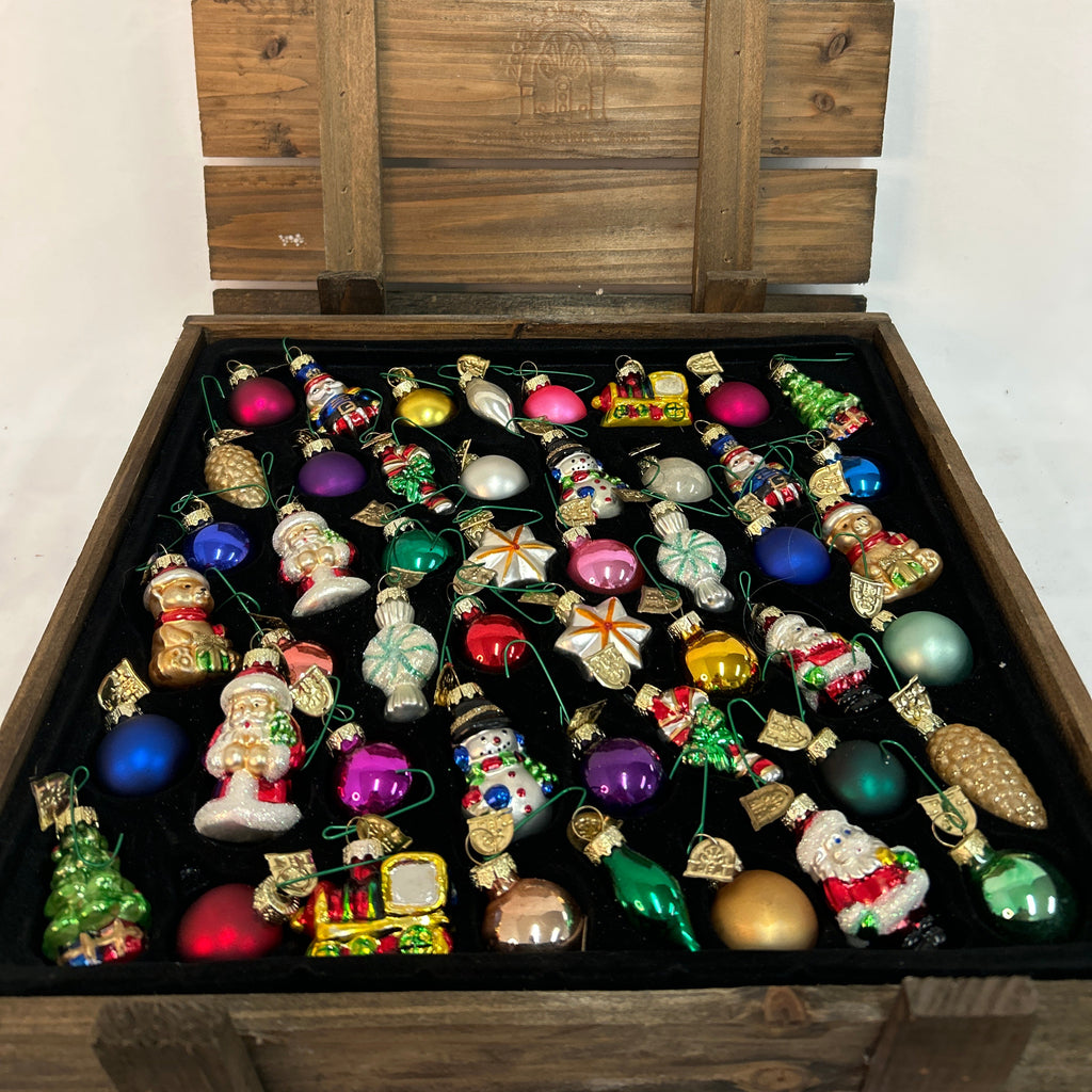 A large wooden crate with its lid propped open, filled with a collection of colorful Christmas ornaments on a black background.