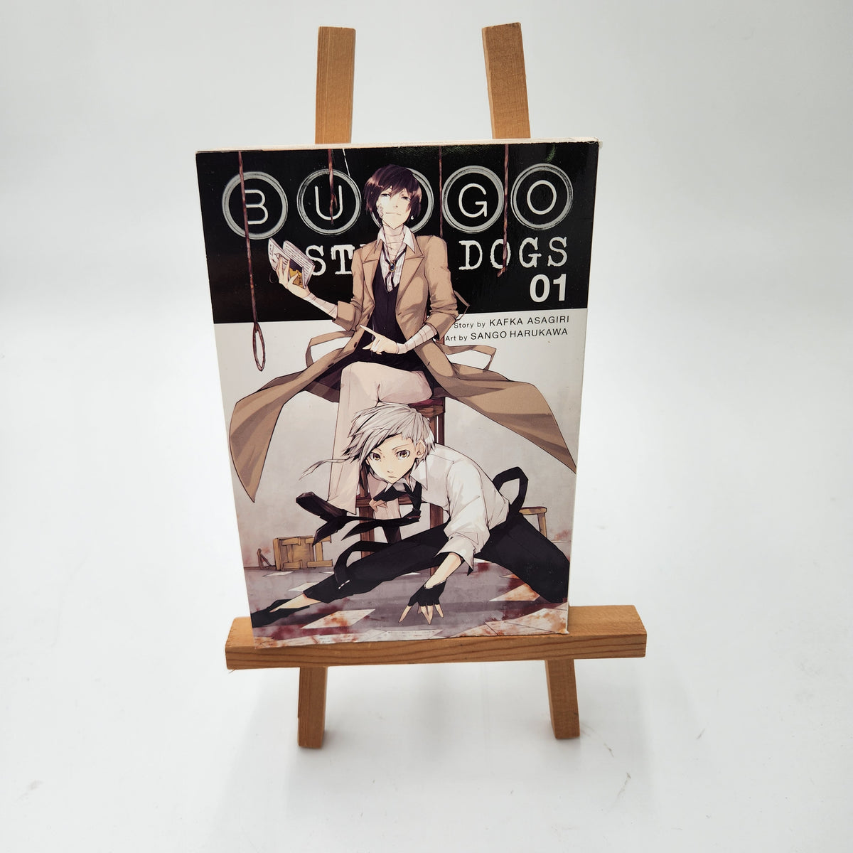 A manga book titled 'BUGS OVER DOGS 01' displayed upright on a small wooden easel against a plain white background.