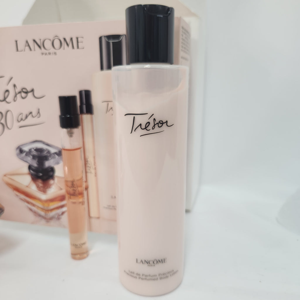 Lancôme Tésor body wash bottle in a pale pink shade with a black cap, shown alongside a matching pink box and two small perfume sample vials on a white surface.