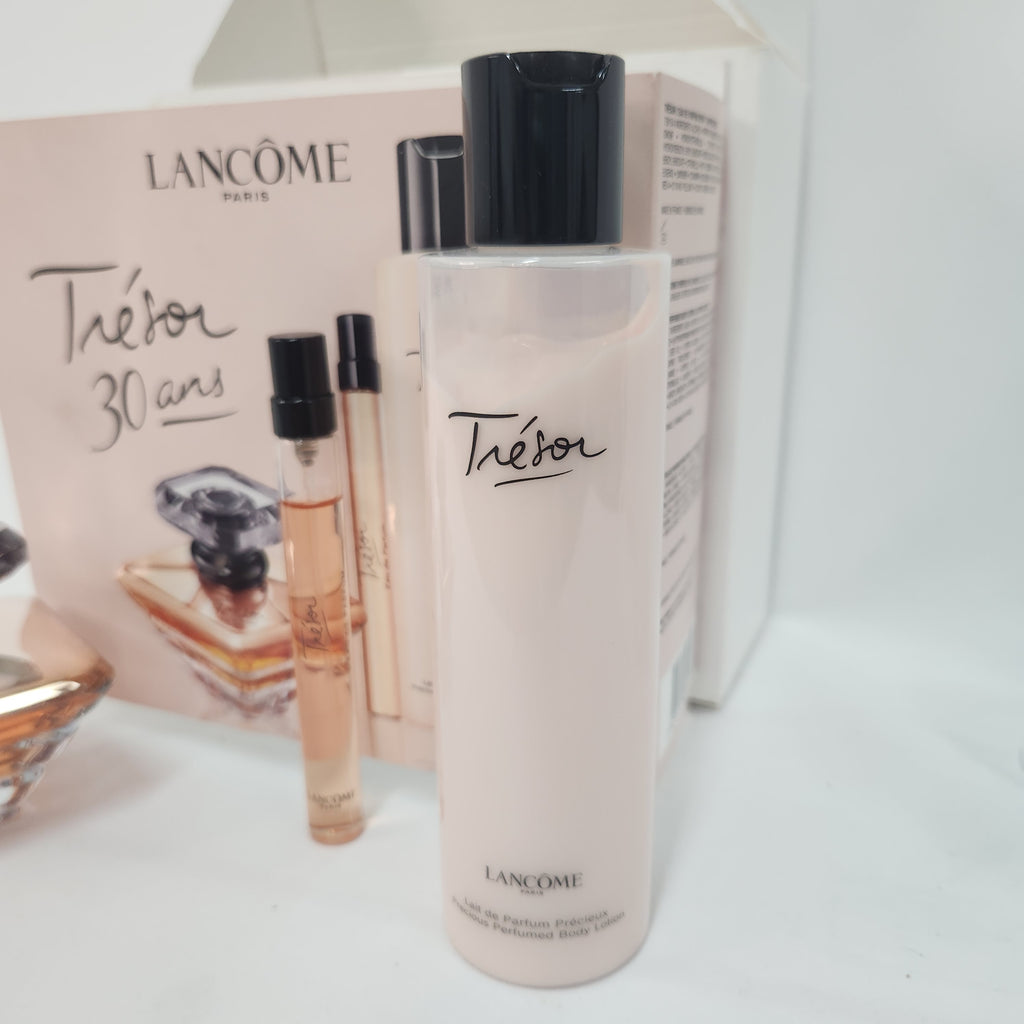 A bottle of Lancôme Théor perfume body wash with a black cap stands in front of its pink and white packaging box and two small sample vials on a white surface.