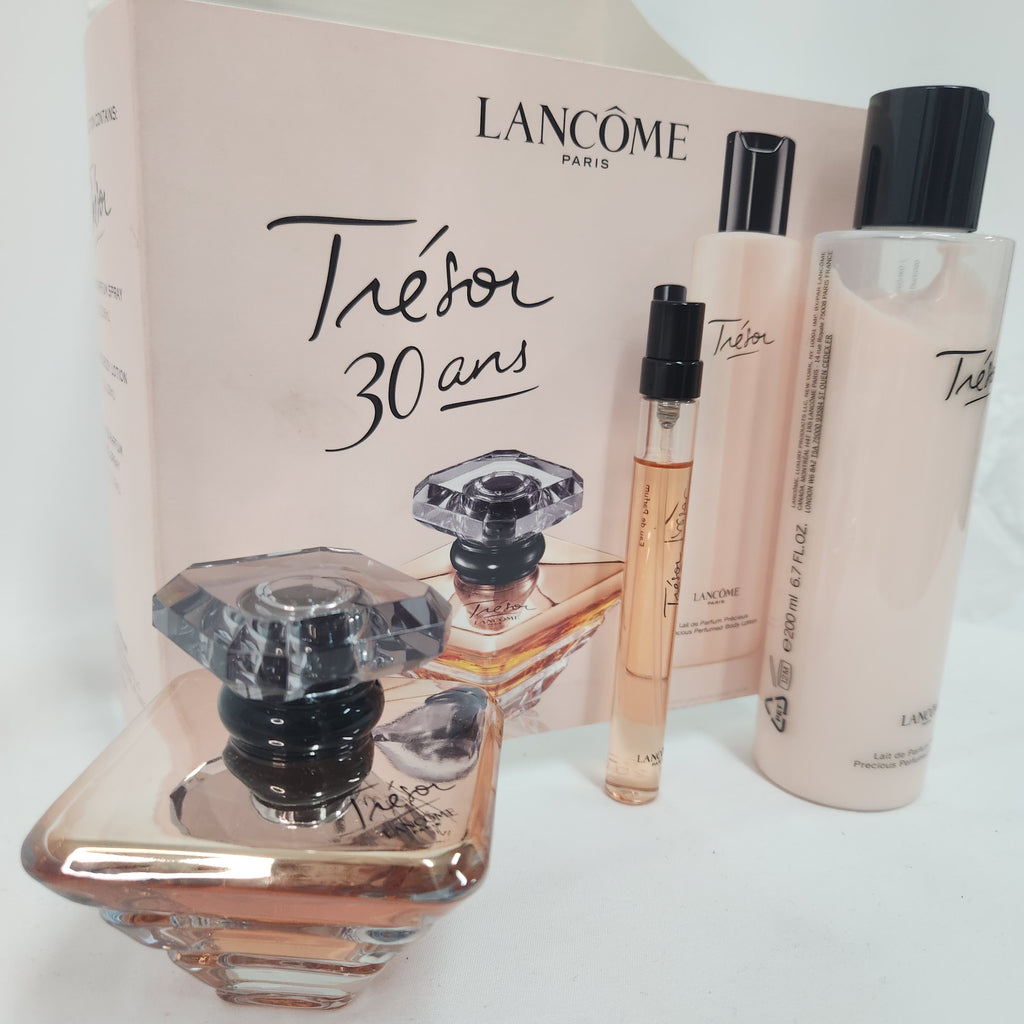 Lancôme Tésor 30 ans perfume gift set featuring a large faceted glass perfume bottle, a small travel spray vial, and a large bottle of matching body wash, all arranged in front of their pale pink branded packaging box.