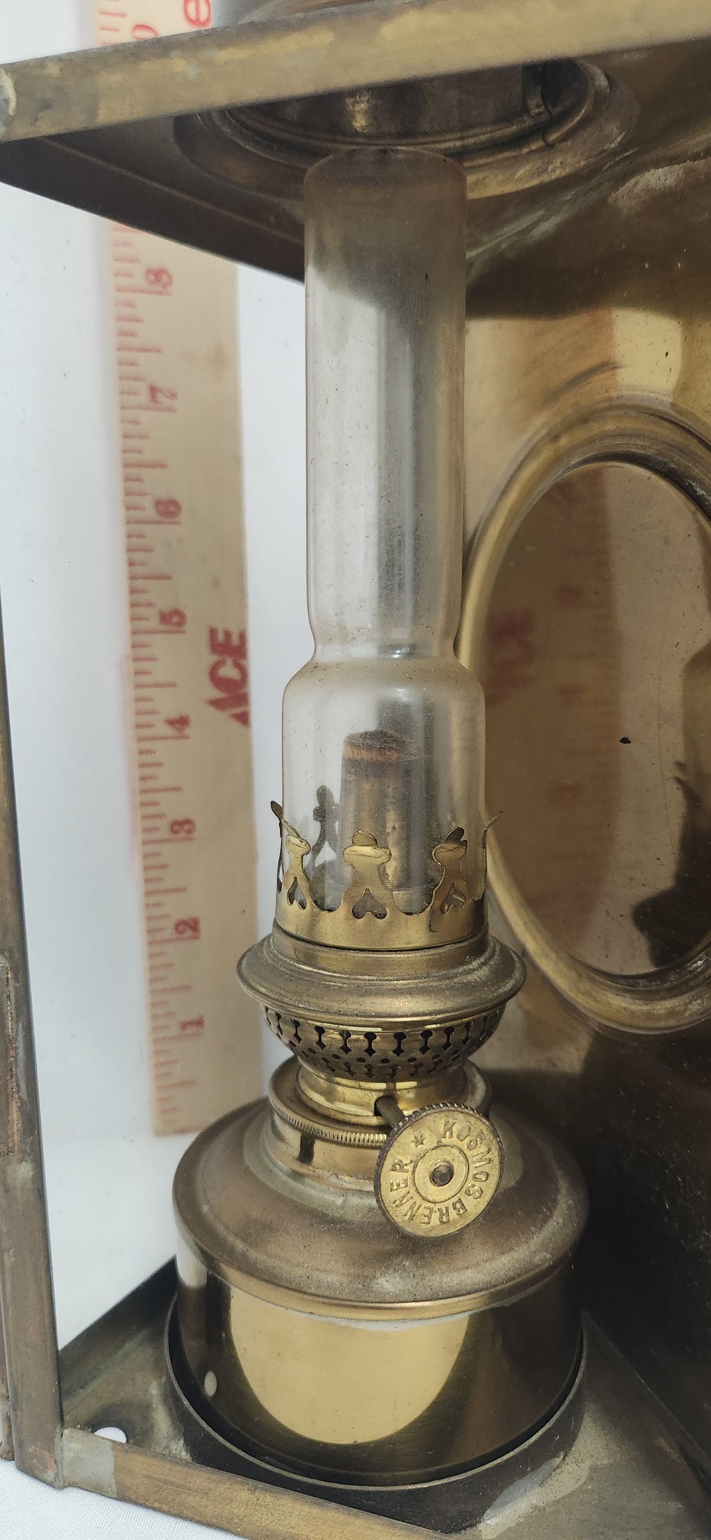 A vintage brass oil lamp with a clear glass chimney and brass base, shown next to a wooden ruler for scale.