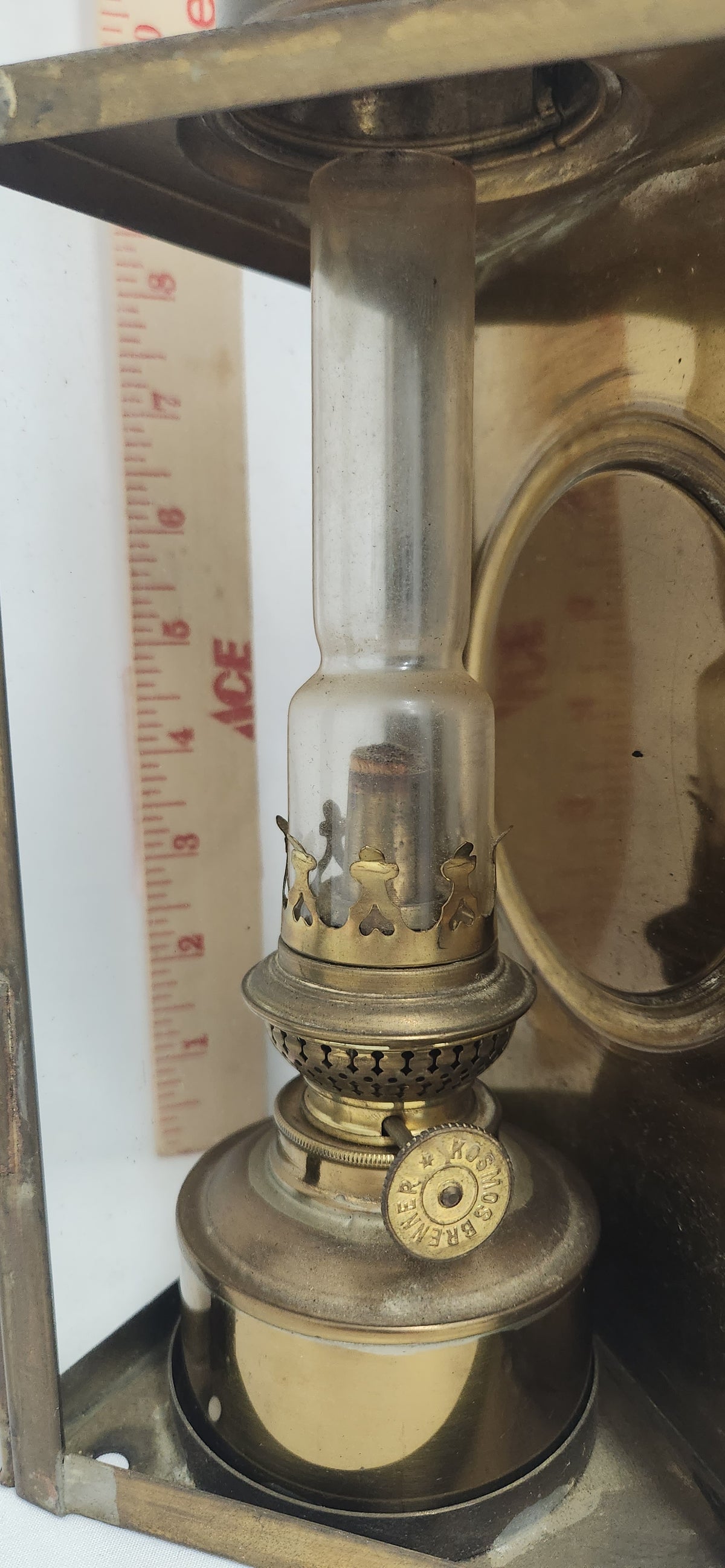 A vintage brass oil lamp with a clear glass chimney and brass base, shown next to a wooden ruler for scale.