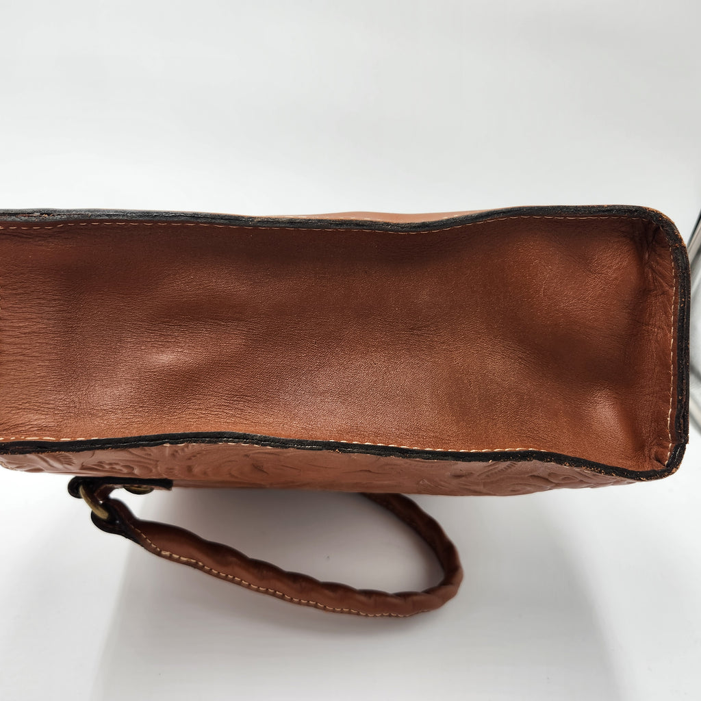 A close-up of a brown leather Patricia Nash handbag showing the interior lining, edge stitching, and part of the braided shoulder strap on a white background.