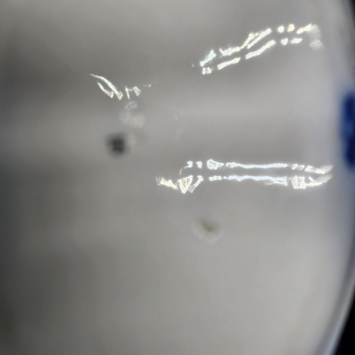 A close-up, slightly blurry view of a light gray or off-white surface with a few small dark spots and bright white reflections. Antique 1890s Flow Blue Cobalt Oval Serving Bowl Deep Vegetable Dish