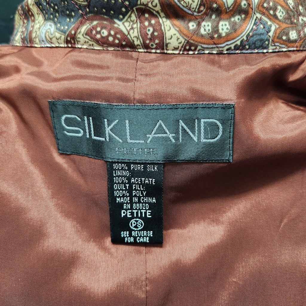 Close-up of the interior label of a Silkland quilted jacket, showing the brand name SILKLAND on a dark gray tag and size information below, set against a warm brown satin lining.