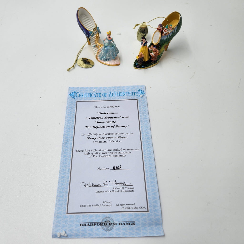 A pair of miniature Cinderella-themed slipper ornaments displayed on a white surface next to a Certificate of Authenticity from Bradford Exchanger. Cinderella Snow White