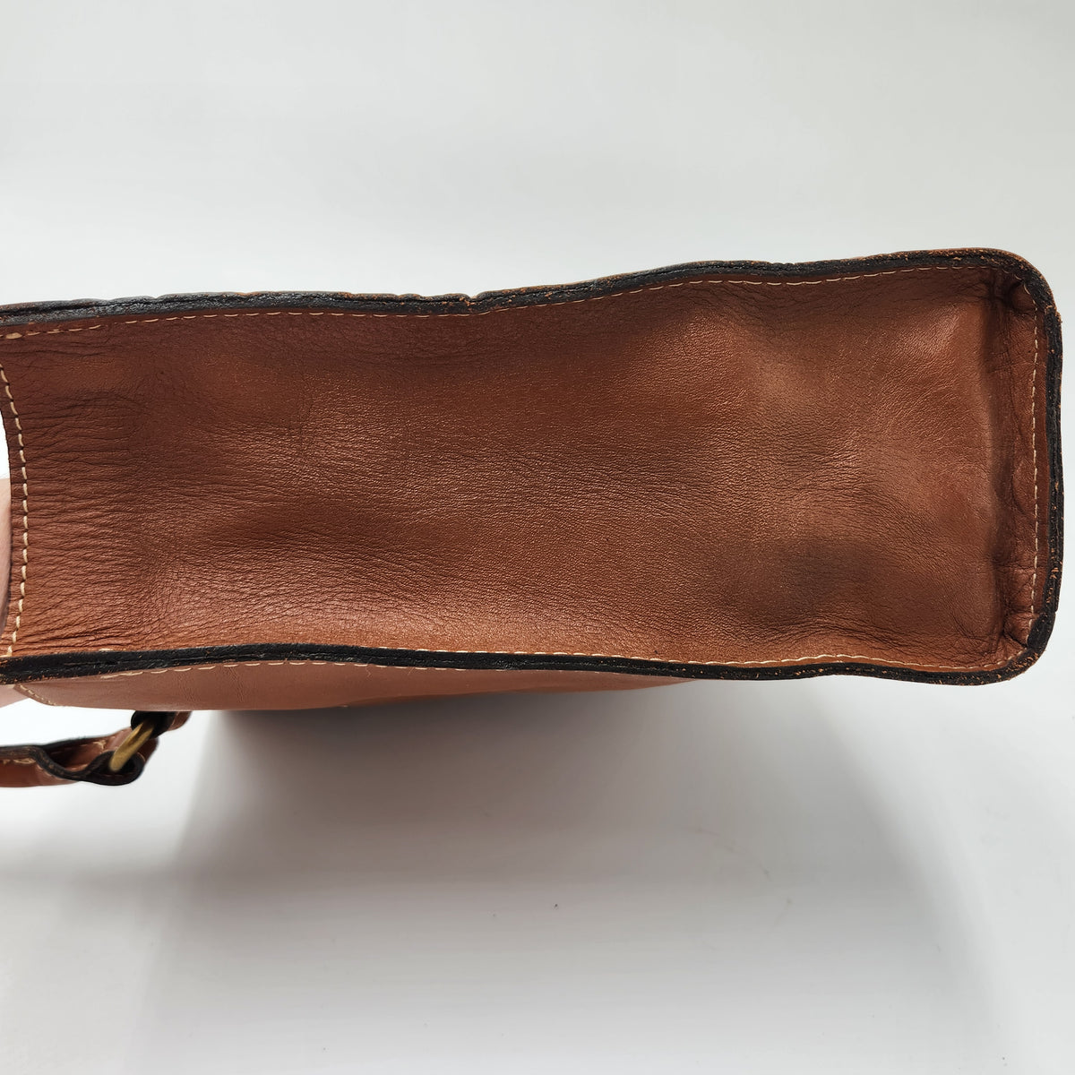 Close-up of the brown leather bottom base and edge of a handbag on a white background. Patricia Nash