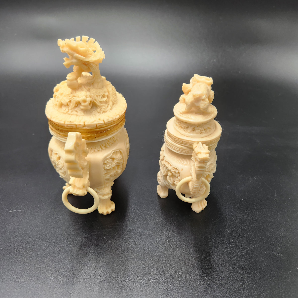 Two cream-colored, intricately carved Chinese dragon figurines or decorative objects displayed side-by-side on a dark gray background. Vintage Chinese Carved Resin Faux Ivory Incense Burners Tripod Censers 