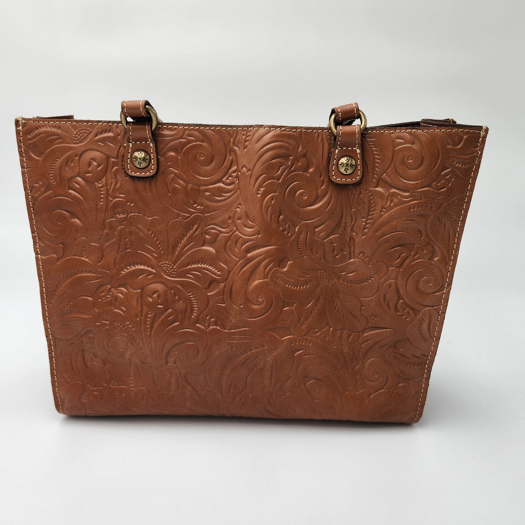 A brown embossed Patricia Nash leather handbag with a western-style floral pattern, featuring two leather strap handles with brass-tone hardware, shown against a neutral light gray background.