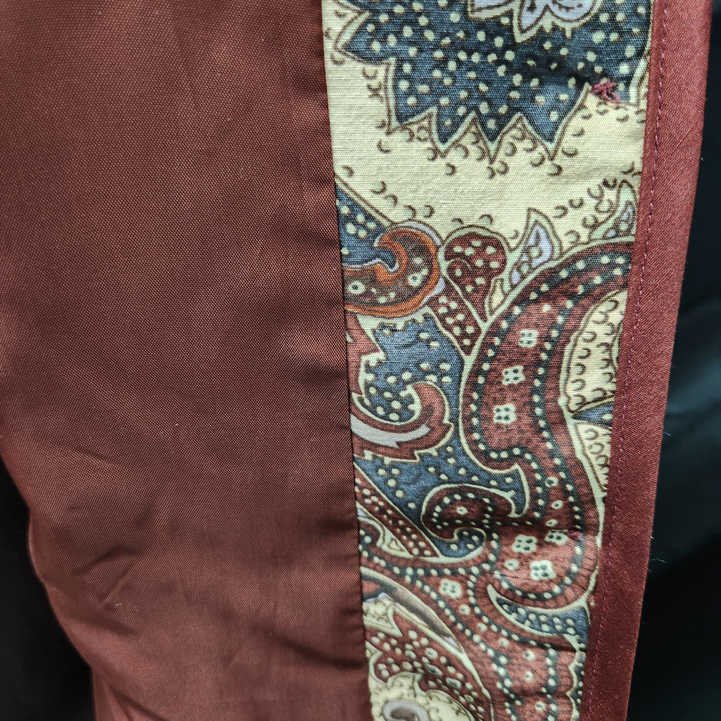 Close-up of a silk garment showing a solid rust-brown fabric panel next to a vertical paisley patterned trim in cream, blue, and rust-brown.