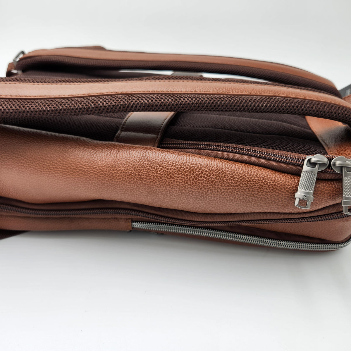 A close-up of a Samsonite brown pebbled leather bag showing its interior compartments, zippers, and dark brown mesh lining on a white background.