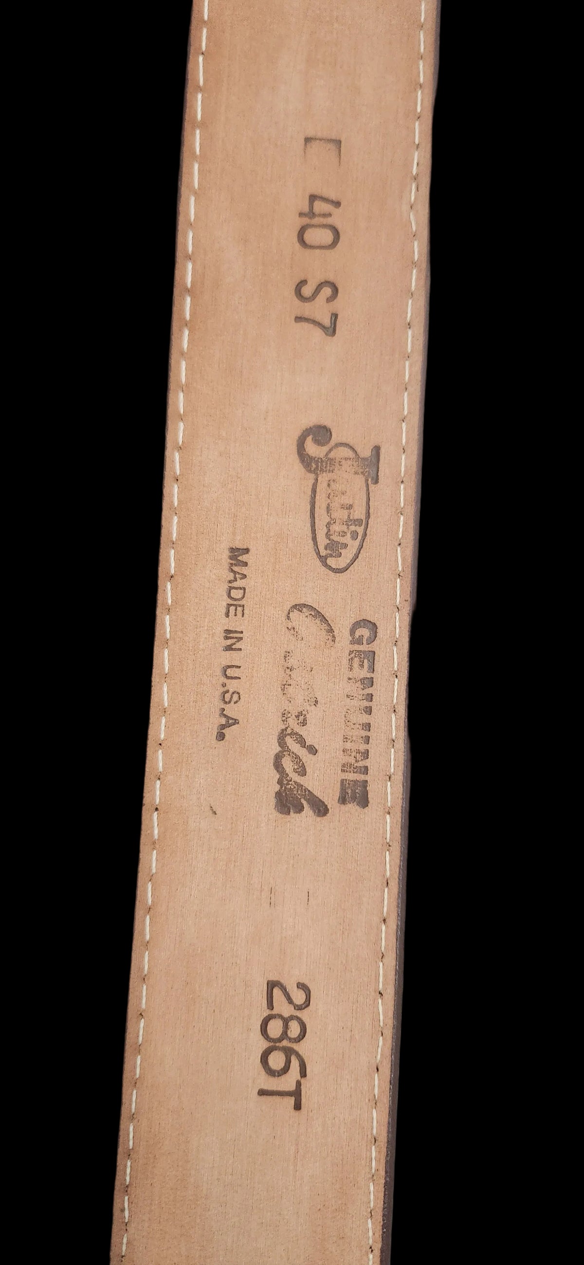 A close-up of a tan leather belt strap showing printed black text and logos, including 'JBL', 'Genuine Leather', 'Made in USA', and '286T'.