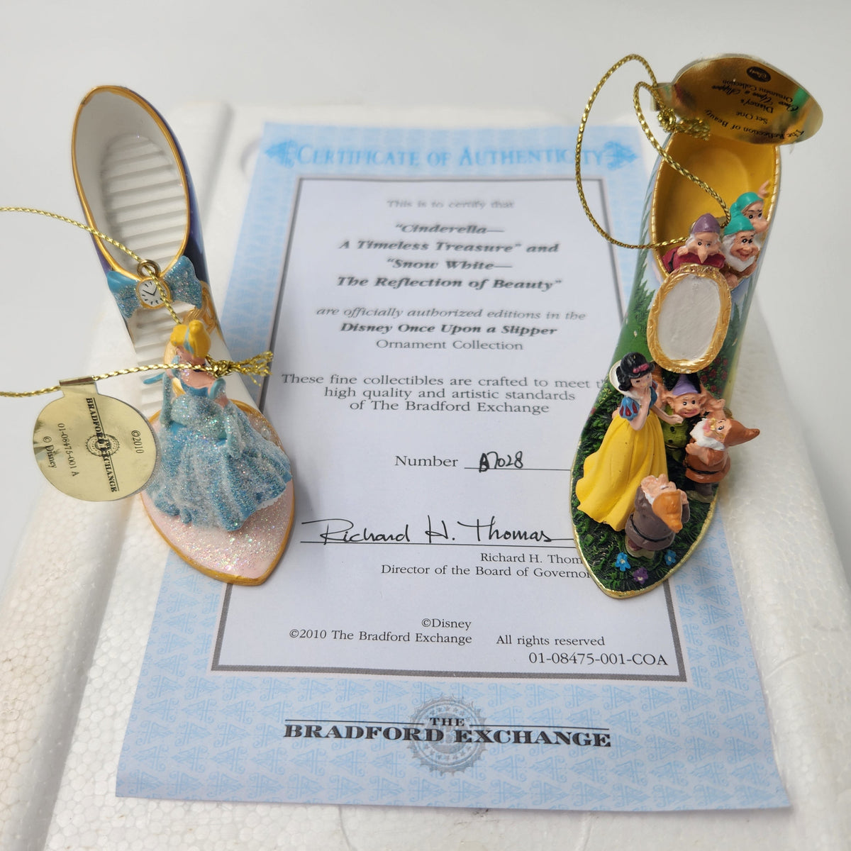 Two Disney-themed miniature collectible shoes displayed on top of a certificate of authenticity. One shoe is light blue with gold trim and a pearl-like embellishment, and the other is green with a yellow dress and colorful character details. Bradford Exchange Cinderella & Snow White 