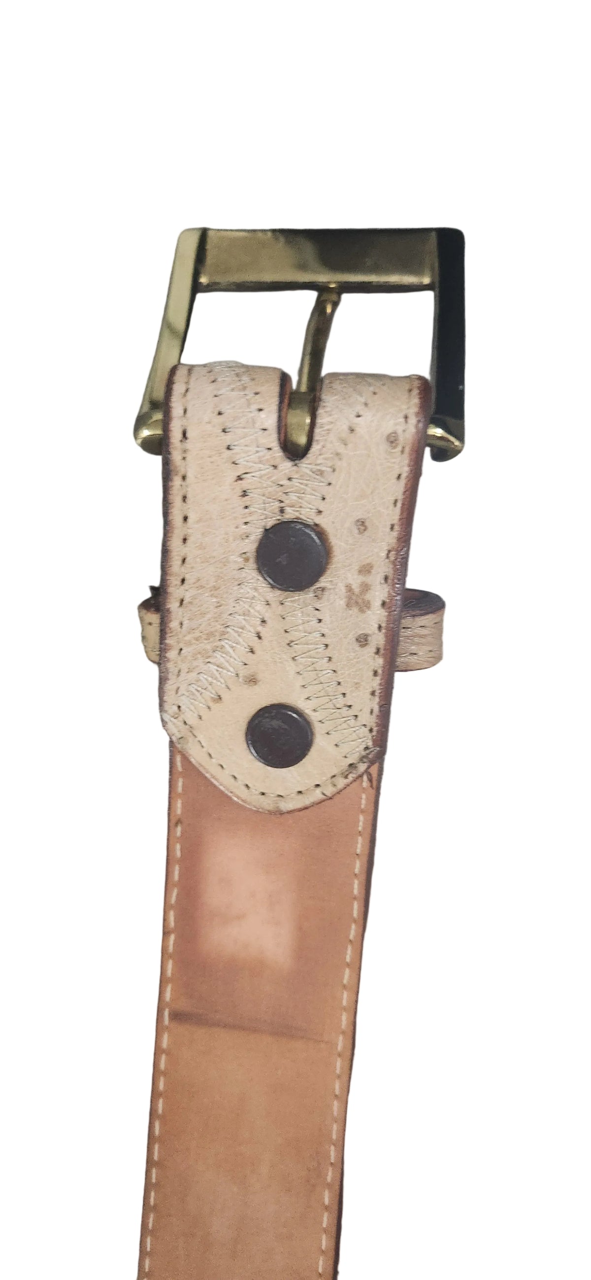 A close-up of a leather belt with a tan leather strap, a textured beige leather keeper tab with two dark metal rivets, and a brass buckle, shown against a plain gray background.Justin Genuine Ostrich Belt
