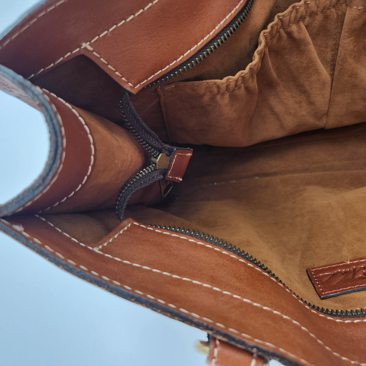 Close-up of the interior of a Patricia Nash brown leather handbag, showing a zippered compartment, interior pockets, contrast stitching, and a small leather brand patch.