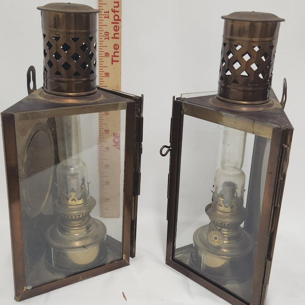 Two vintage oil lanterns with dark bronze metal frames and clear glass panels, shown side by side with a wooden ruler for scale against a white background.