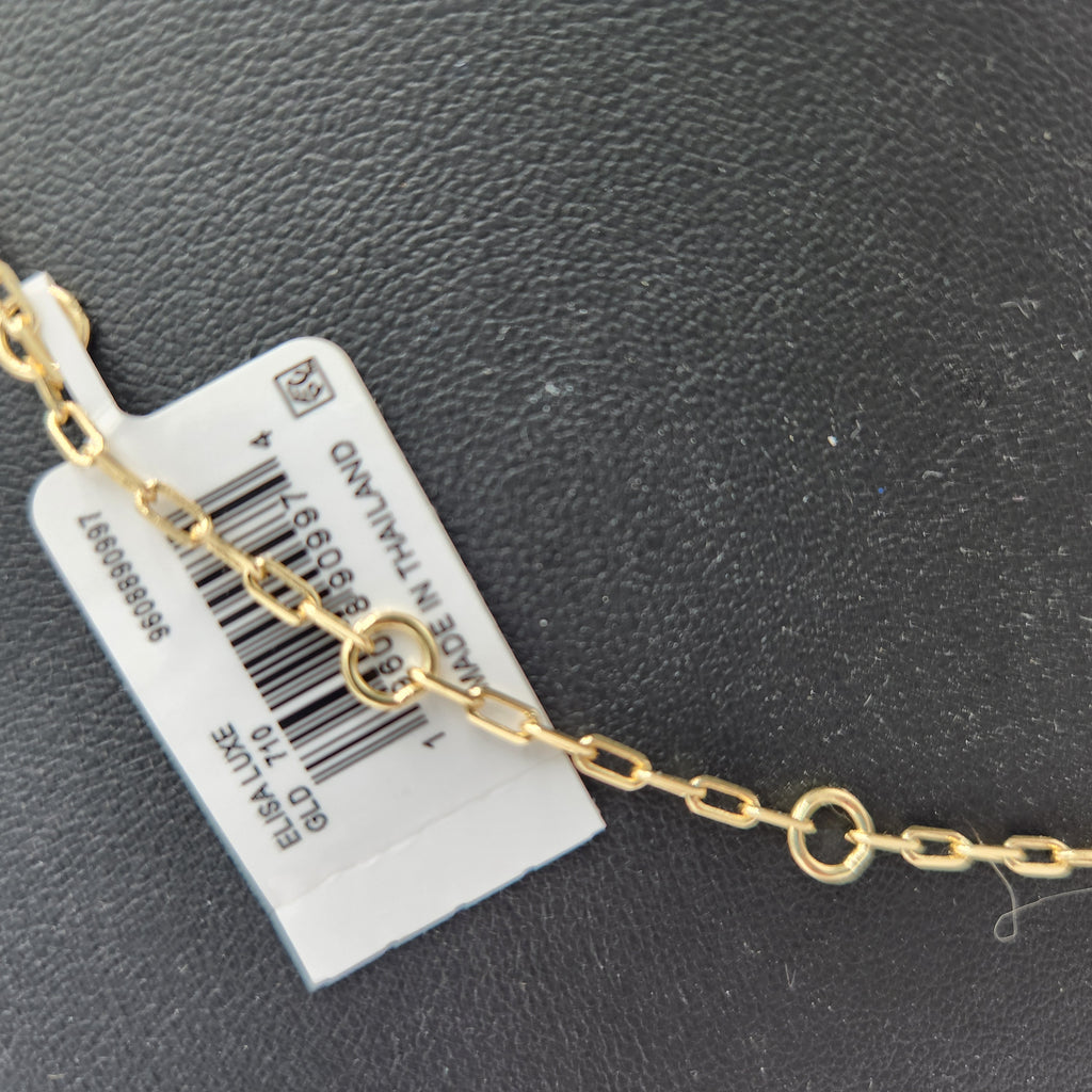 A close-up of a gold chain necklace with a white barcode tag attached, placed on a dark textured surface. Kendra Scott 