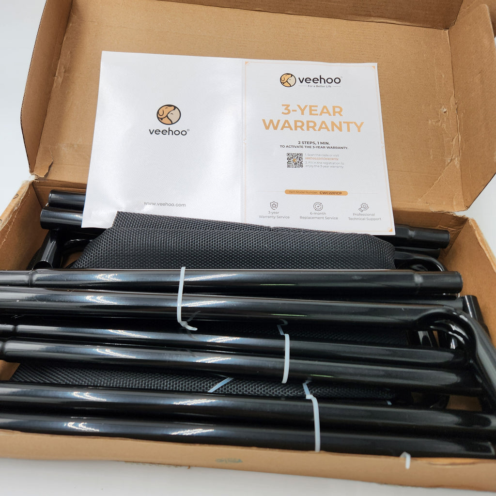 A boxed set of black metal folding frame components, including tubes and a black mesh pad, arranged inside a brown cardboard box with a white Veehoo warranty card on top. Veehoo elevated dog bed