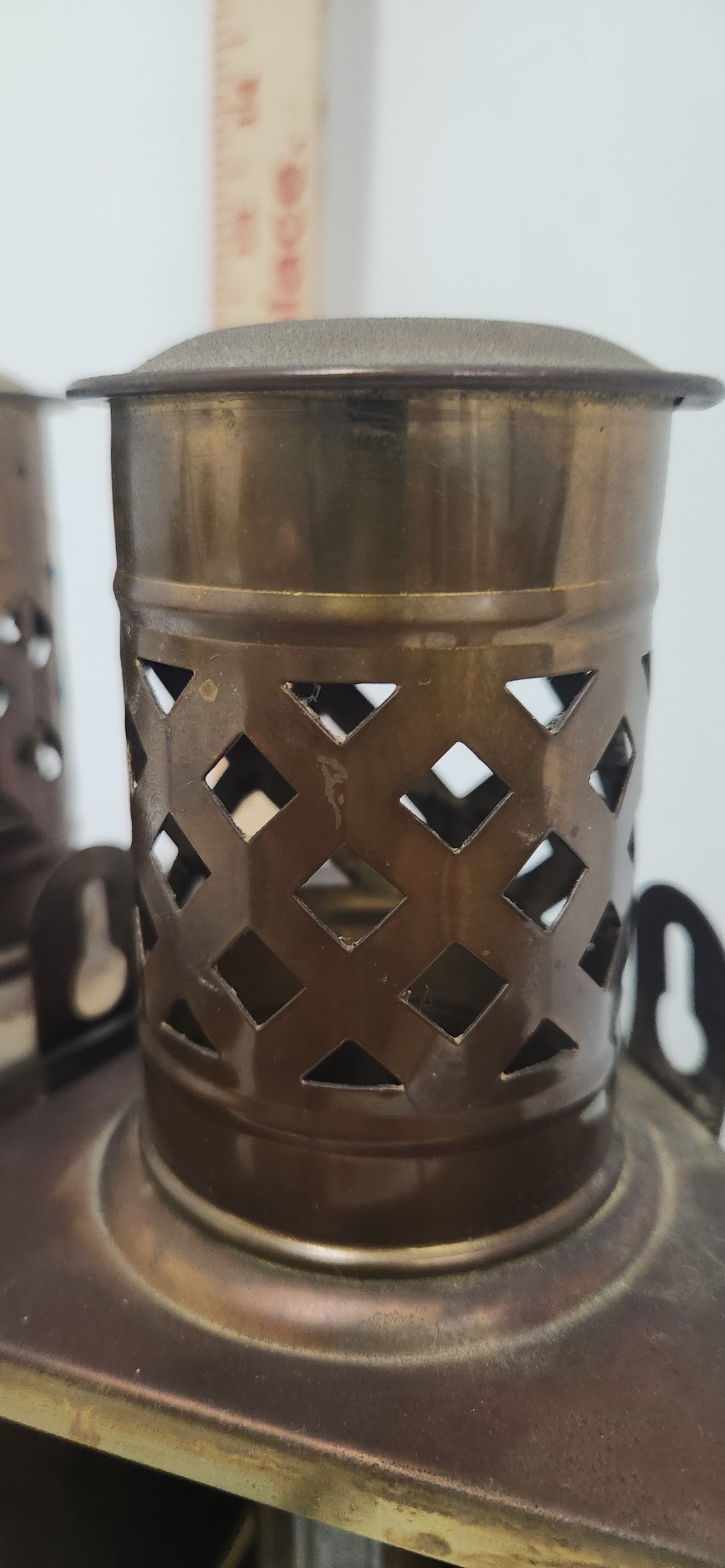 A close-up of a cylindrical metal container with a perforated diamond-pattern cutout body and a domed lid, shown on a shelf.