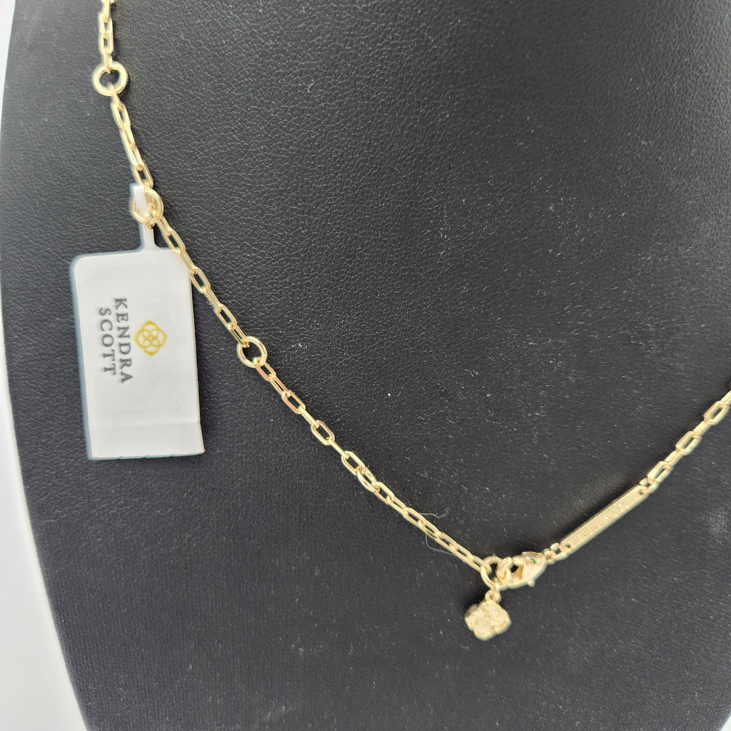 A  Kendra Scott gold chain necklace with a small textured cube charm, displayed on a black jewelry bust next to a Kendra Scott tag.