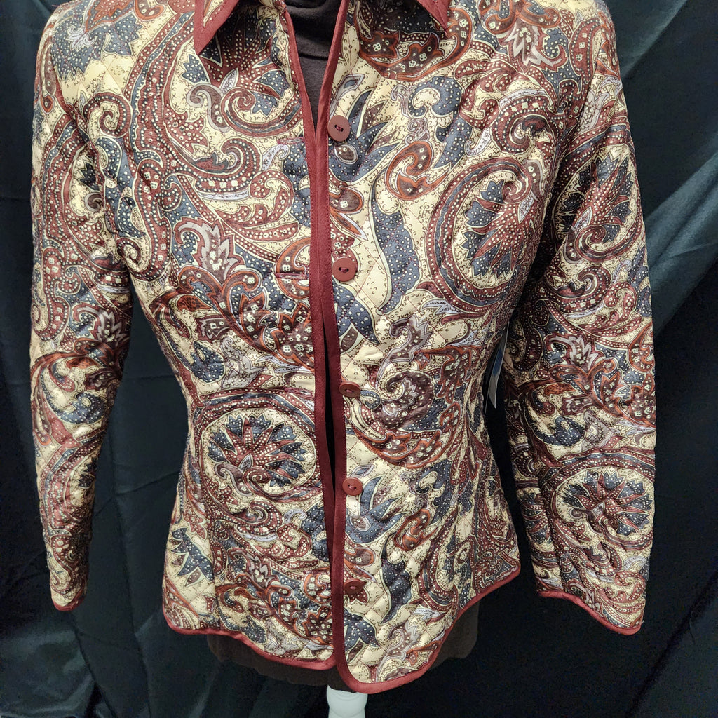 A long-sleeve button-front shirt jacket with an intricate paisley pattern in beige, rust red, and blue, displayed on a mannequin against a black fabric backdrop.