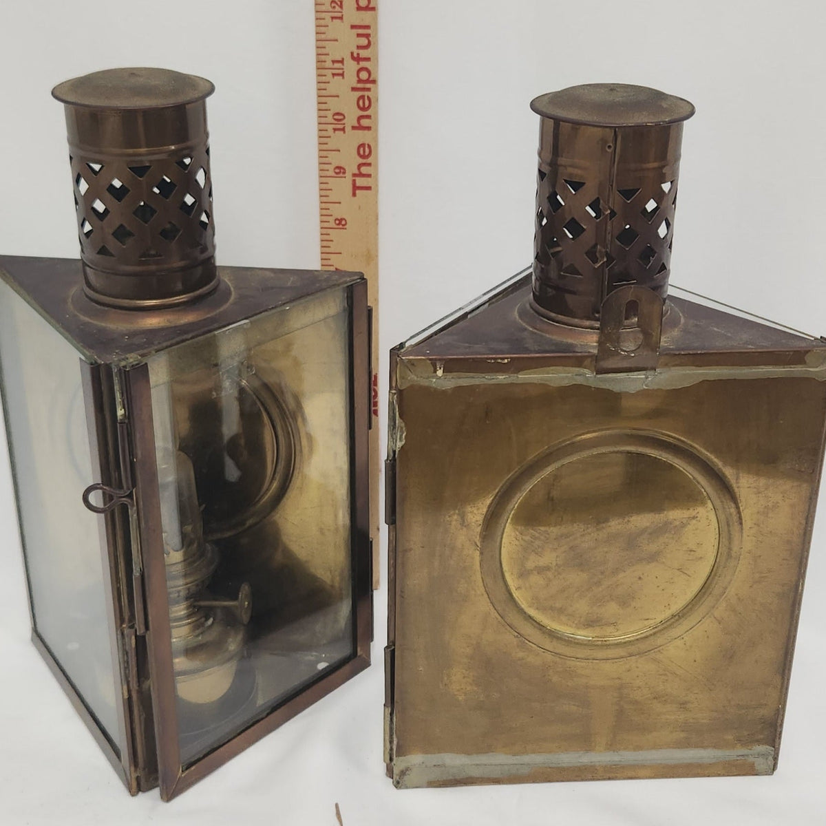 Two vintage brass lanterns with glass panels and perforated metal tops, shown next to a wooden ruler for scale on a white background.