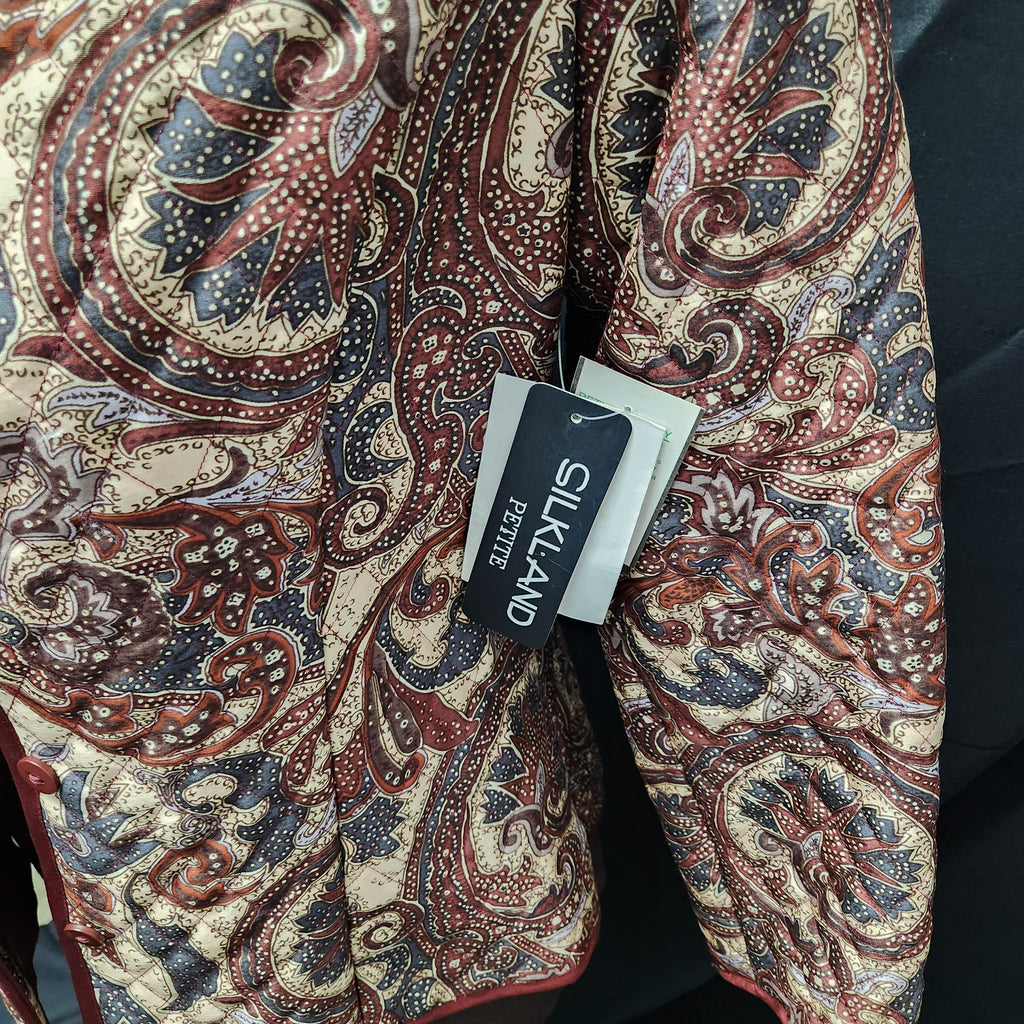 A close-up of a patterned silkland jacket with a paisley design in beige, red, and navy blue, featuring a black Silkland Boutique brand tag.