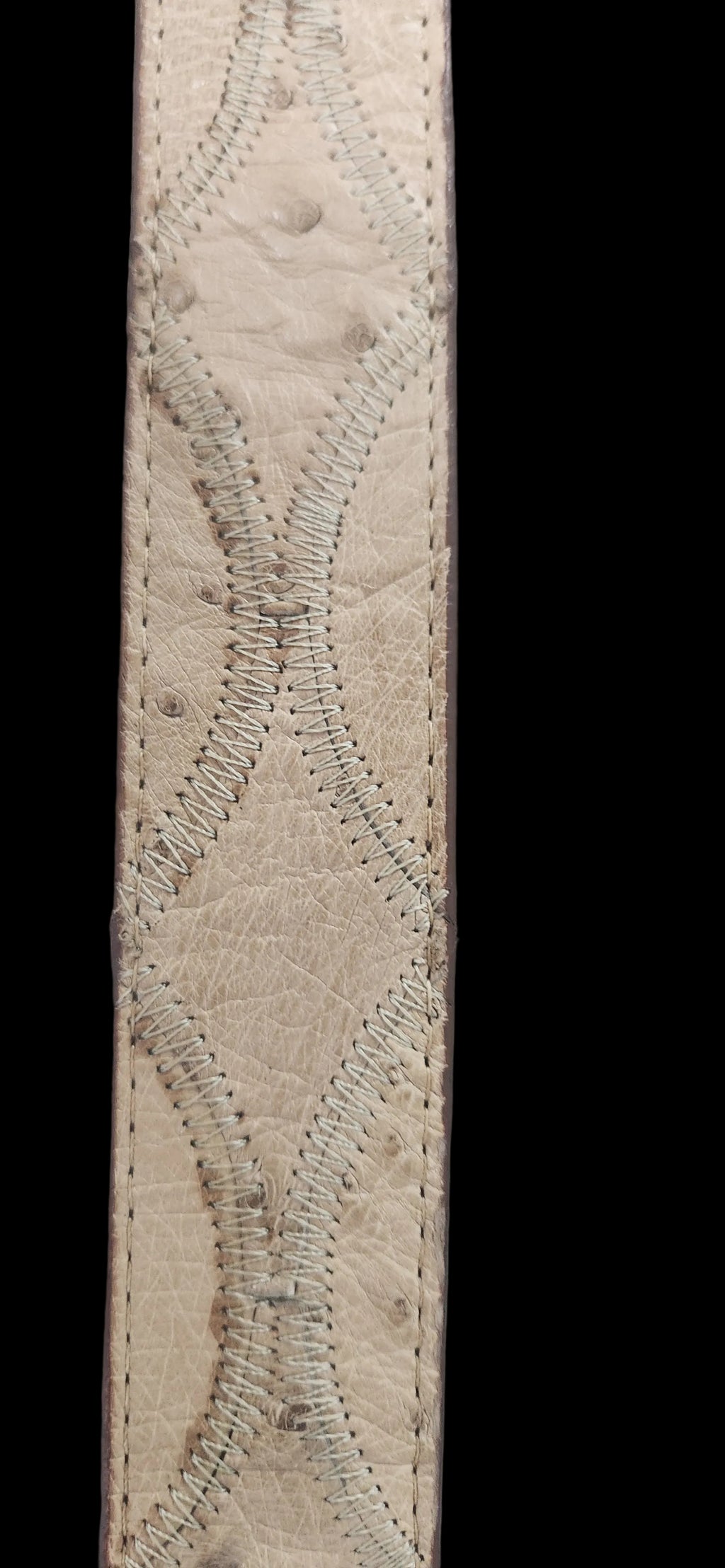 A close-up of a beige ostrich leather strap featuring a textured diamond pattern with decorative whipstitching, set against a dark gray background.