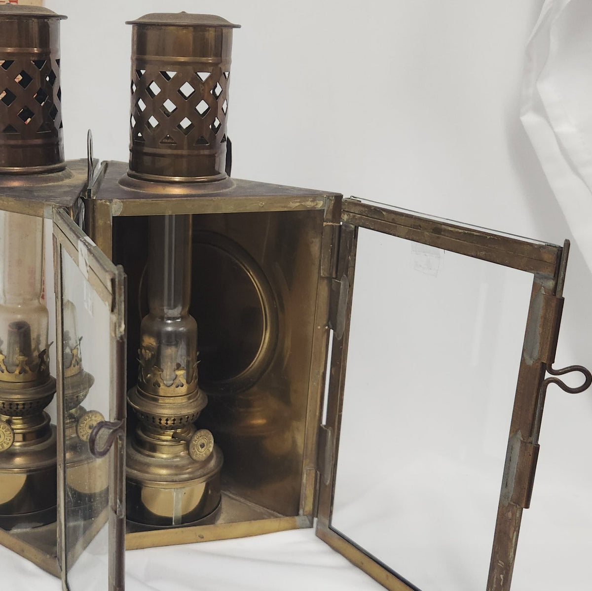 A vintage brass oil lantern with glass doors swung open, showing an antique brass oil lamp inside. The lantern features a cutout metal top and a dark metal frame, photographed against a white studio background.