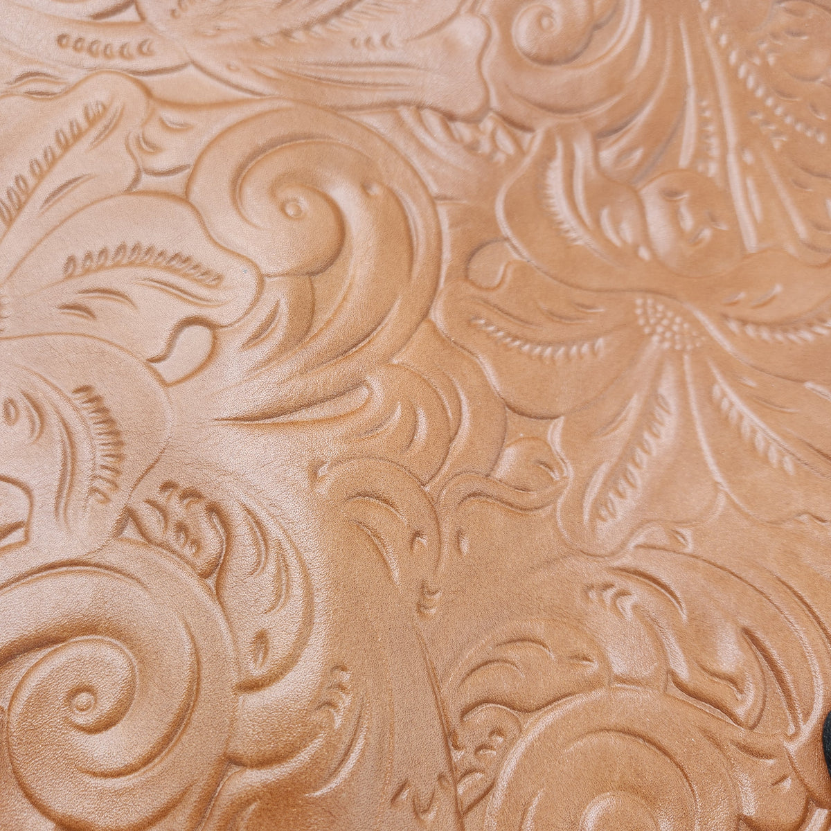 A close-up of a tan leather surface with embossed floral and scrollwork tooling of a Patricia Nash Hand bag.