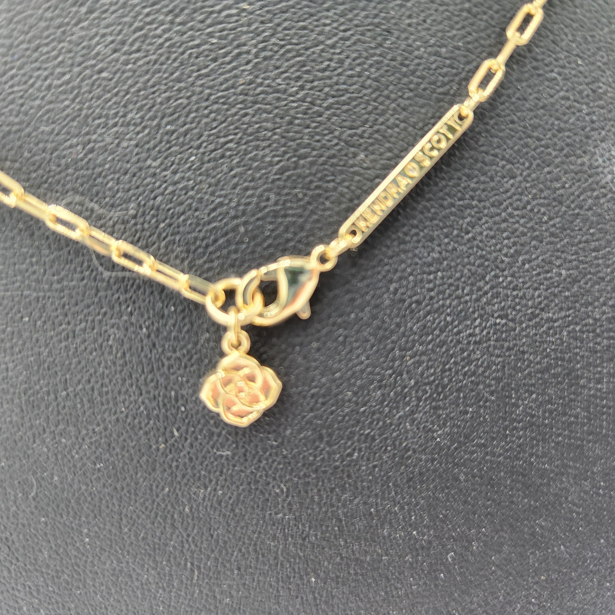 A gold Kendra Scott chain necklace with a lobster clasp, a rose-shaped charm, and a bar engraved with 'M. MURPHY & CO.
