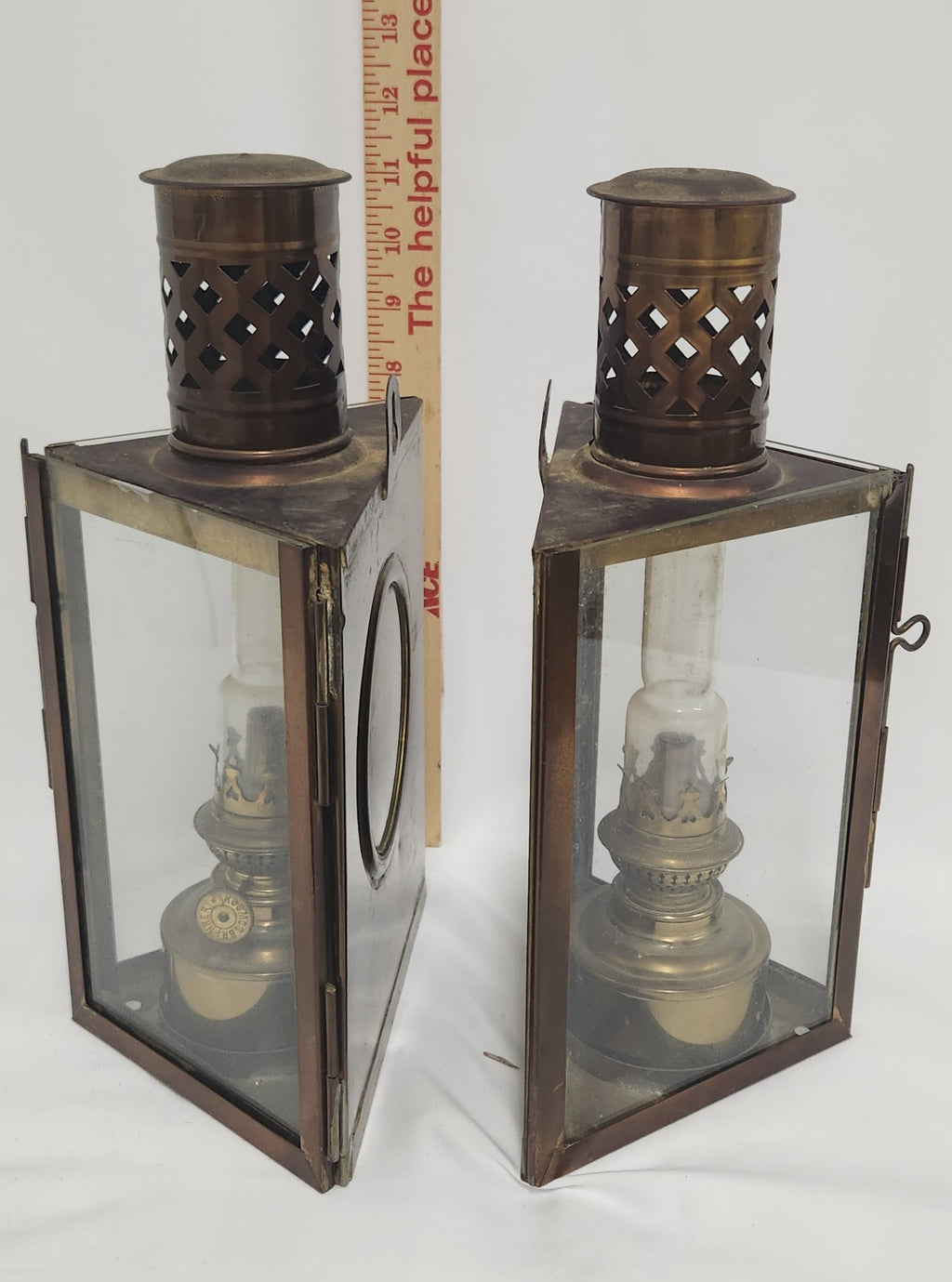 A pair of vintage metal lanterns with glass panels and perforated tops, shown next to a wooden ruler for scale on a white background.