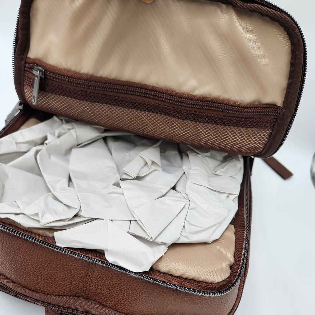 An open brown leather zippered case or organizer filled with crumpled white tissue paper, shown against a plain white background.