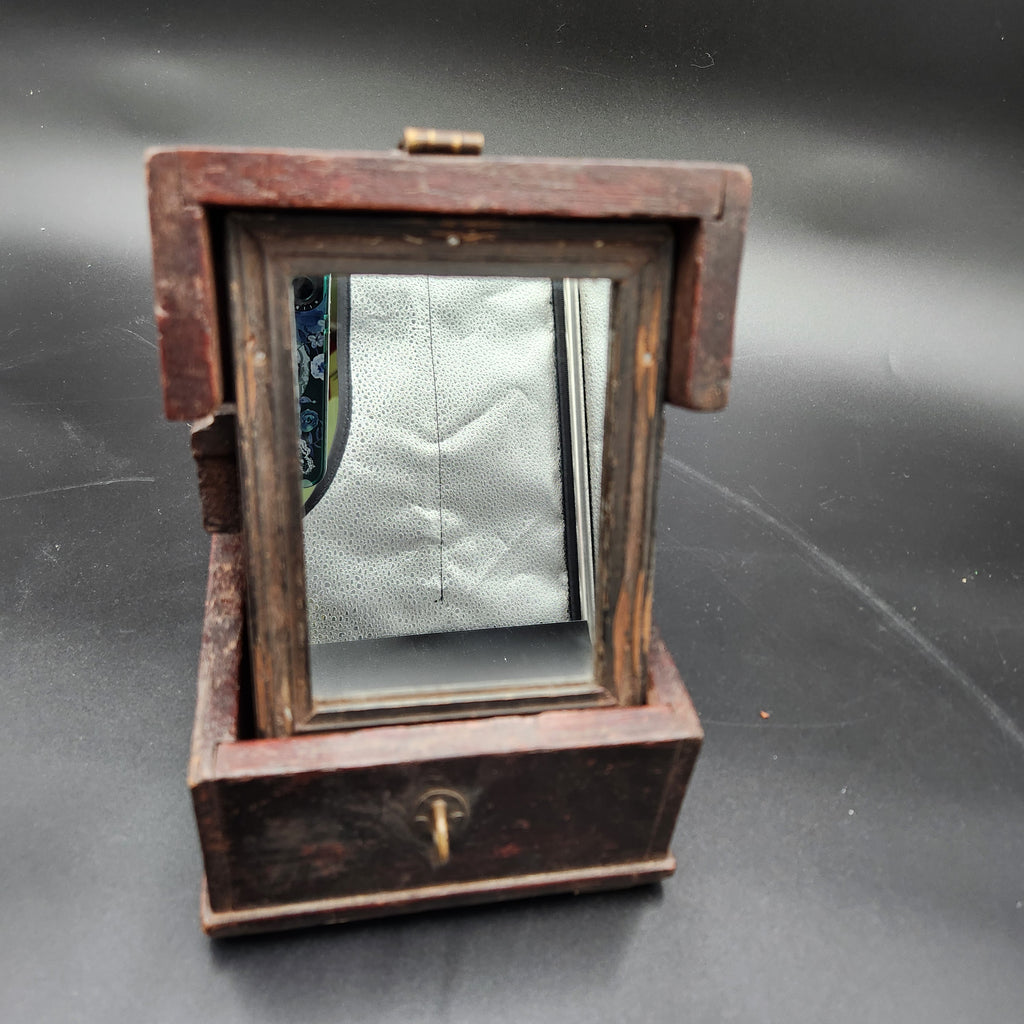 A vintage wooden folding mirror with a dark brown wood frame and a small brass hinge, shown open against a dark gray background.